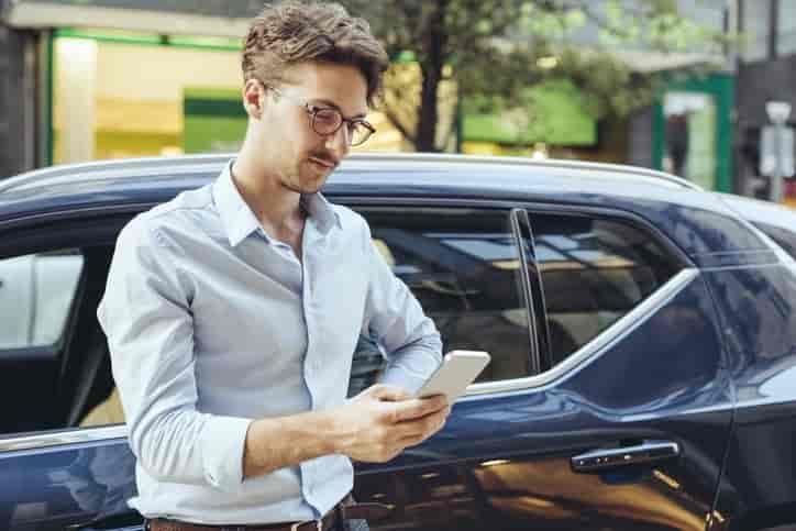 Homme adossé à sa voiture qui consulte son téléphone