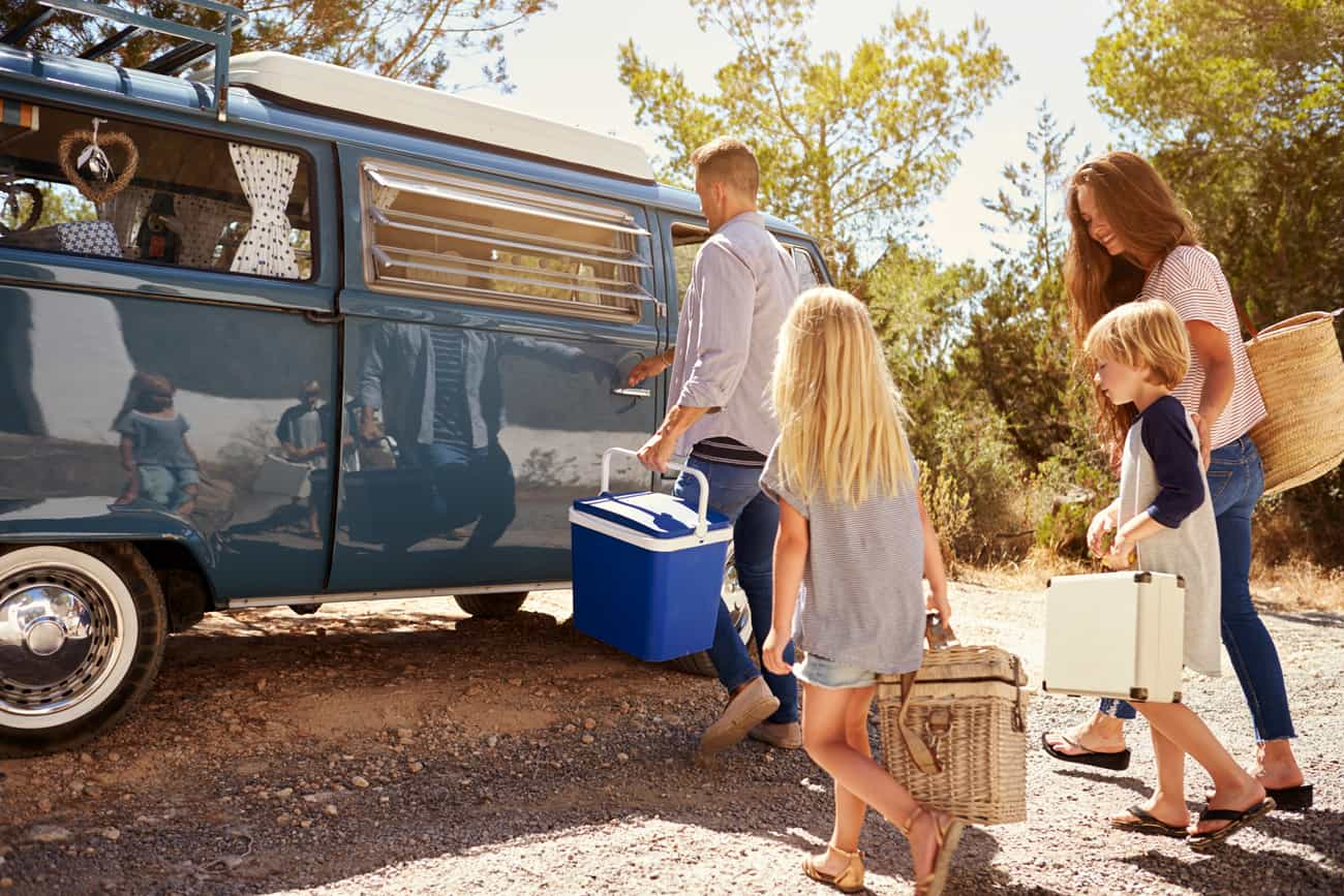 Famille se dirigeant vers un camping-car avec des sacs de pique-nique