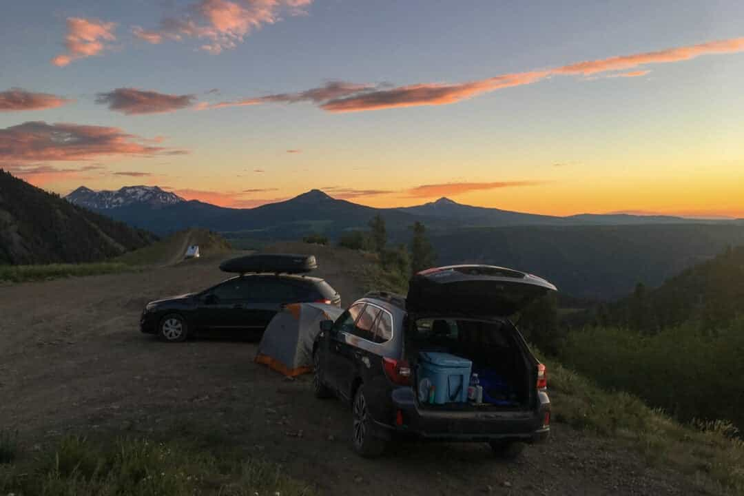 Deux voitures garées surplombent une montagne pittoresque à côté d'une tente dressée