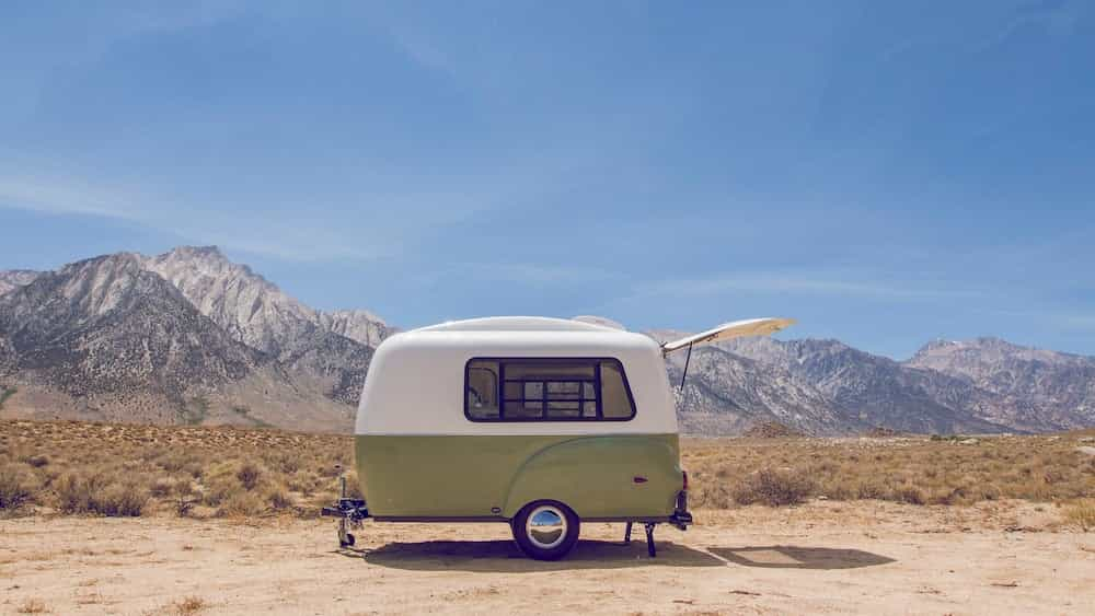 Green and white vintage camper with mountains in background