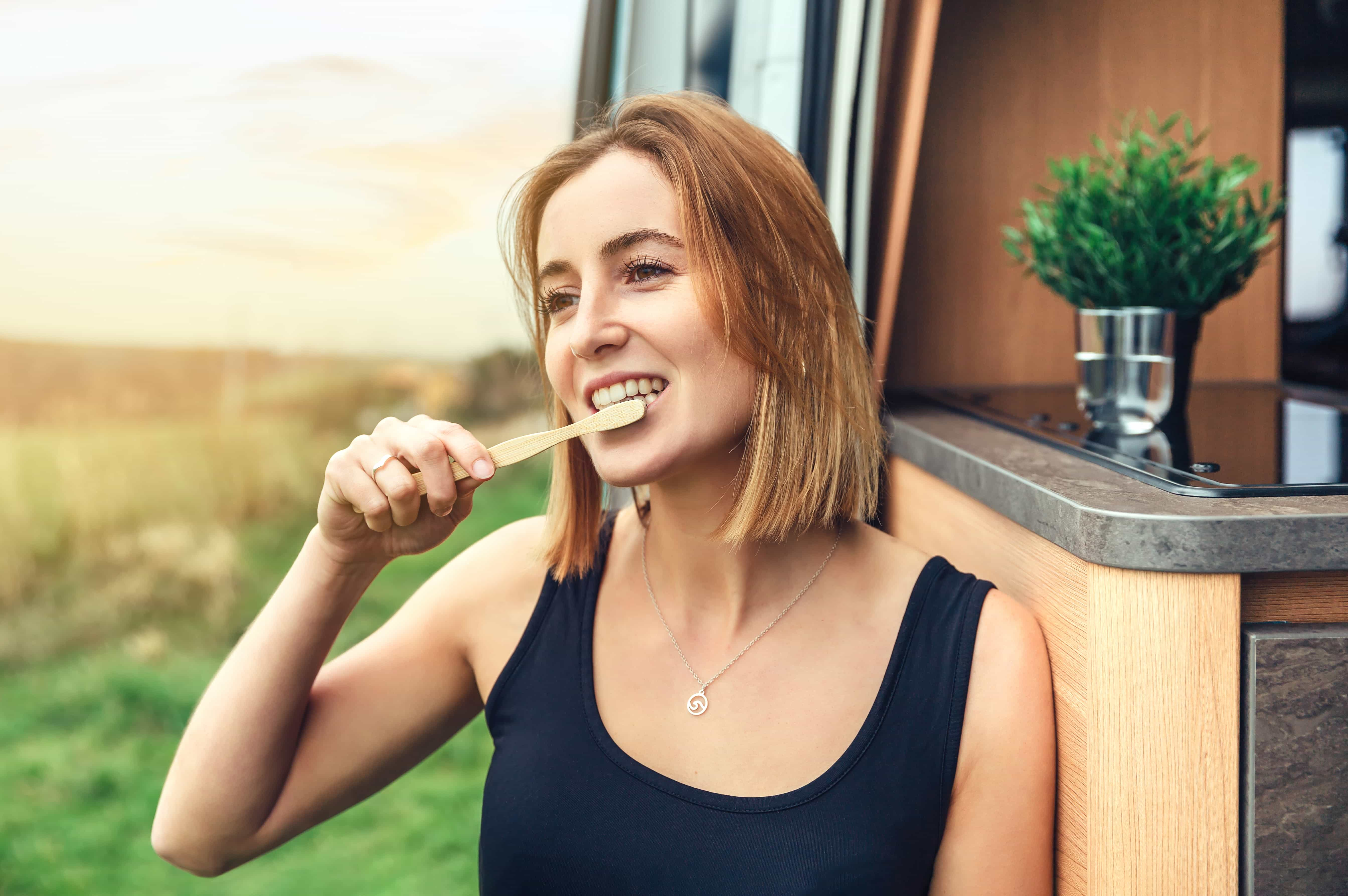 Young woman brushing her teeth with a bamboo toothbrush outdoors in the morning during a camper van trip.